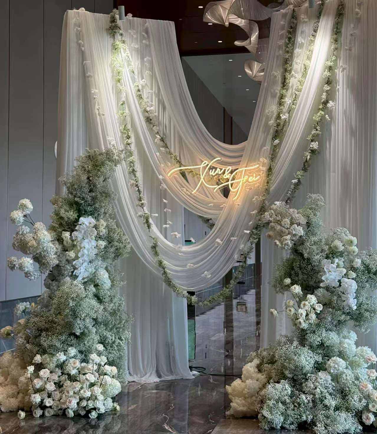 Commercial-grade white chiffon sheer curtains and silk flower arch stands for luxury wedding stage decoration.